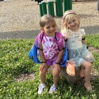 Two CDLC children sitting close together on a playground stump, smiling